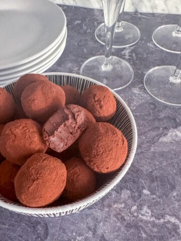 Dark chocolate boozy truffles in a bowl next to plates and wine glasses.