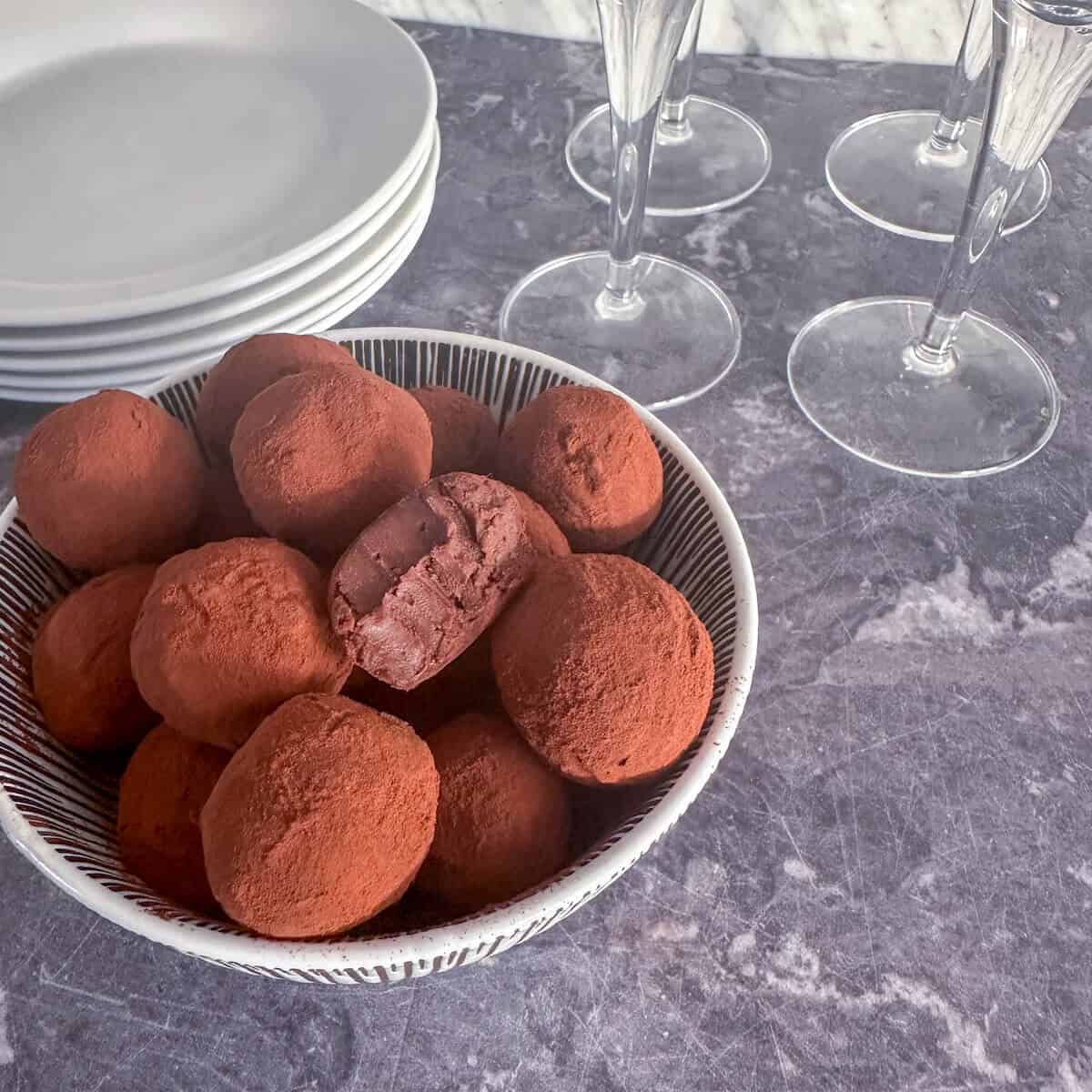 Dark chocolate boozy truffles in a bowl next to plates and wine glasses. 