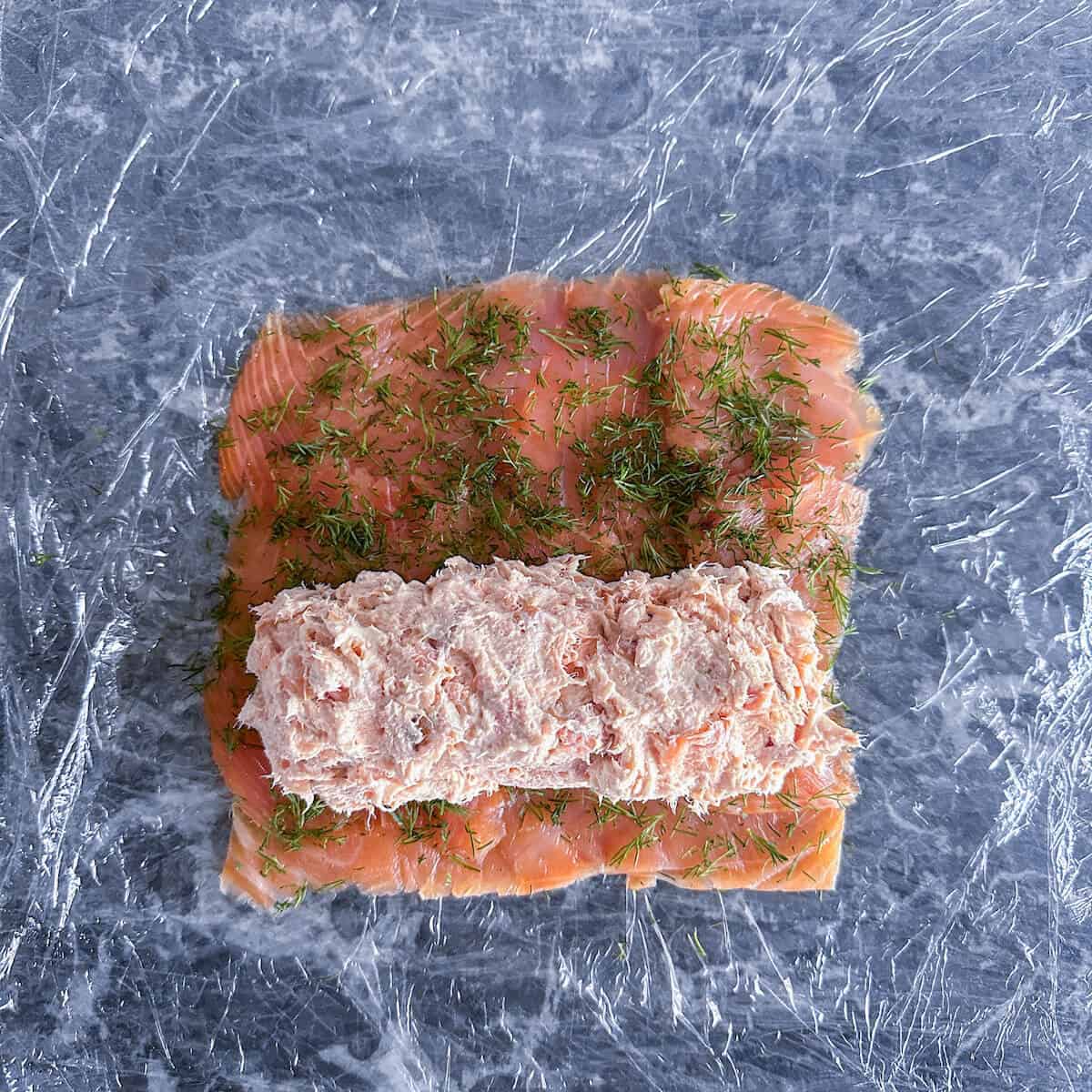 Smoked fish terrine filling placed on top of smoked salmon slices, about to be rolled up. 