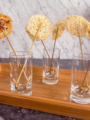 Parmesan lollipops in clusters in tall shot glasses on a tray.