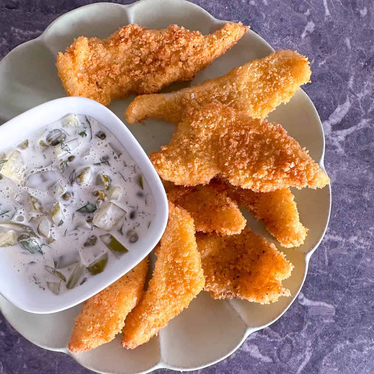 Homemade fresh fish goujons on a plate with a bowl of tartare sauce.
