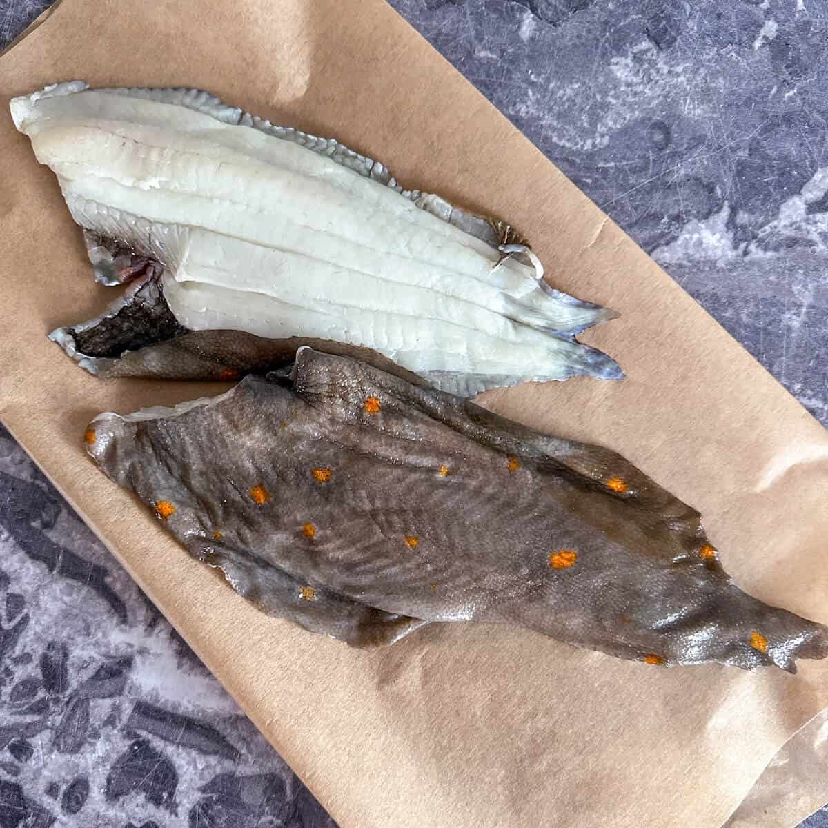 Fresh white fish fillets lying on brown parchment paper. 