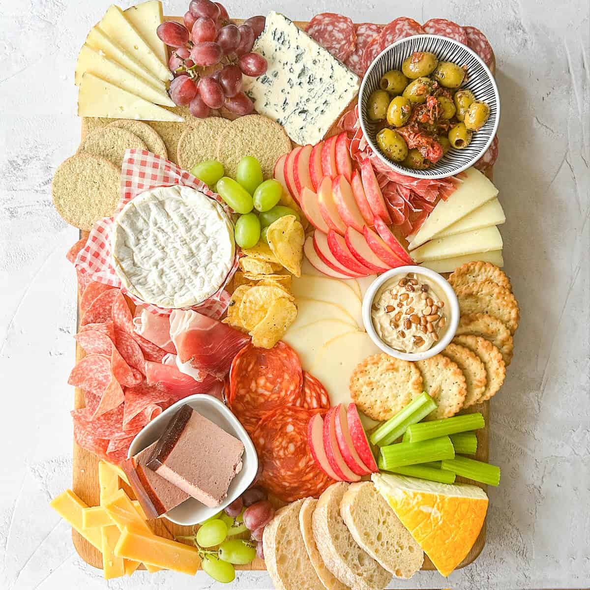 A grazing board with cured meats, cheeses, crackers, grapes, apples, olives, pate, bread and hummus.  
