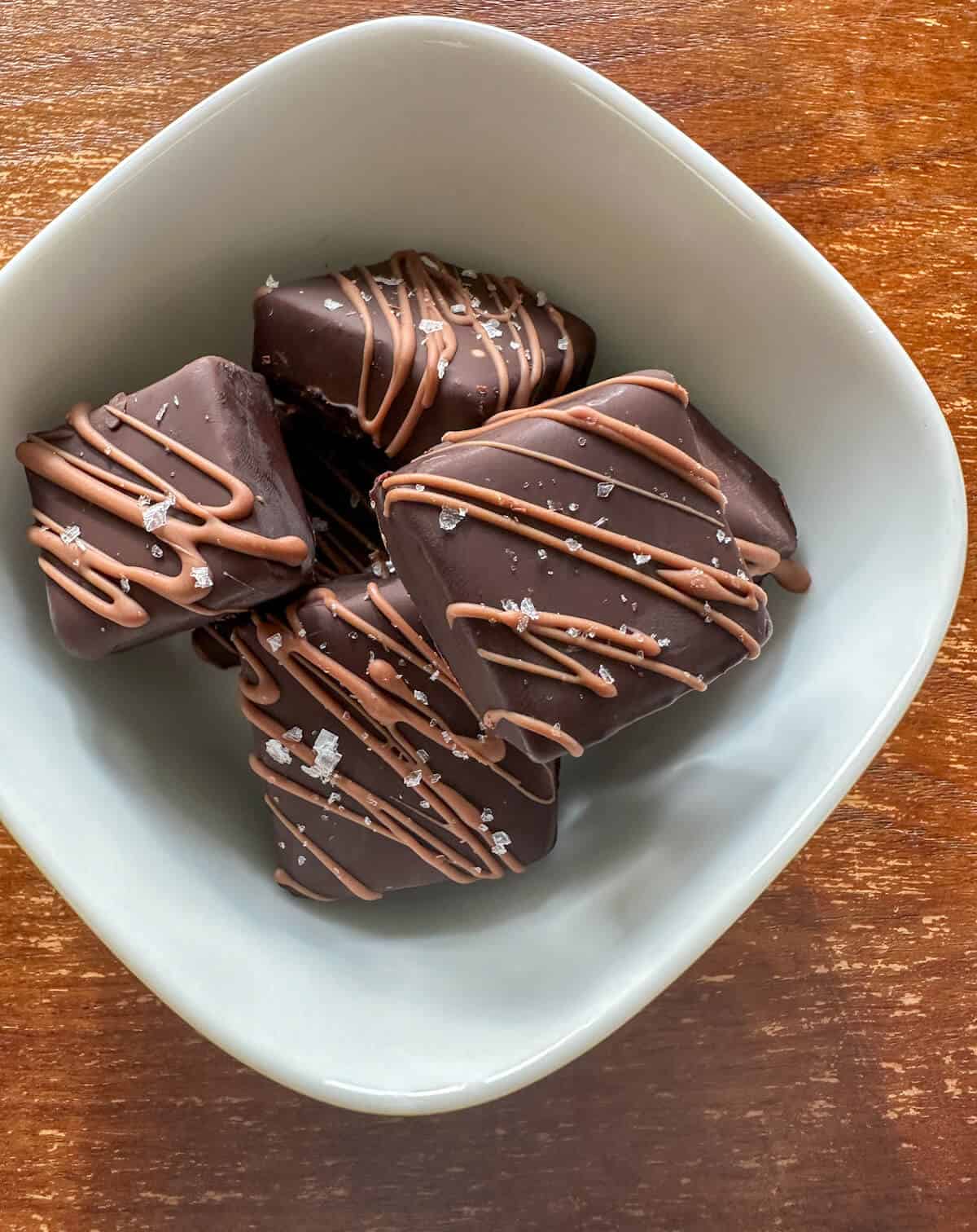 A small bowl full of square chocolate truffles decorated with milk chocolate and sea salt flakes. 