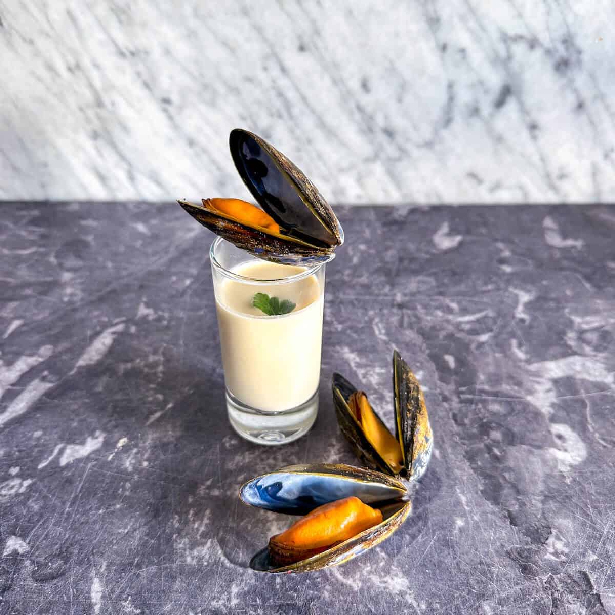Steamed mussels soup amuse bouche in a shot glass with a cooked mussel in the shell on top.