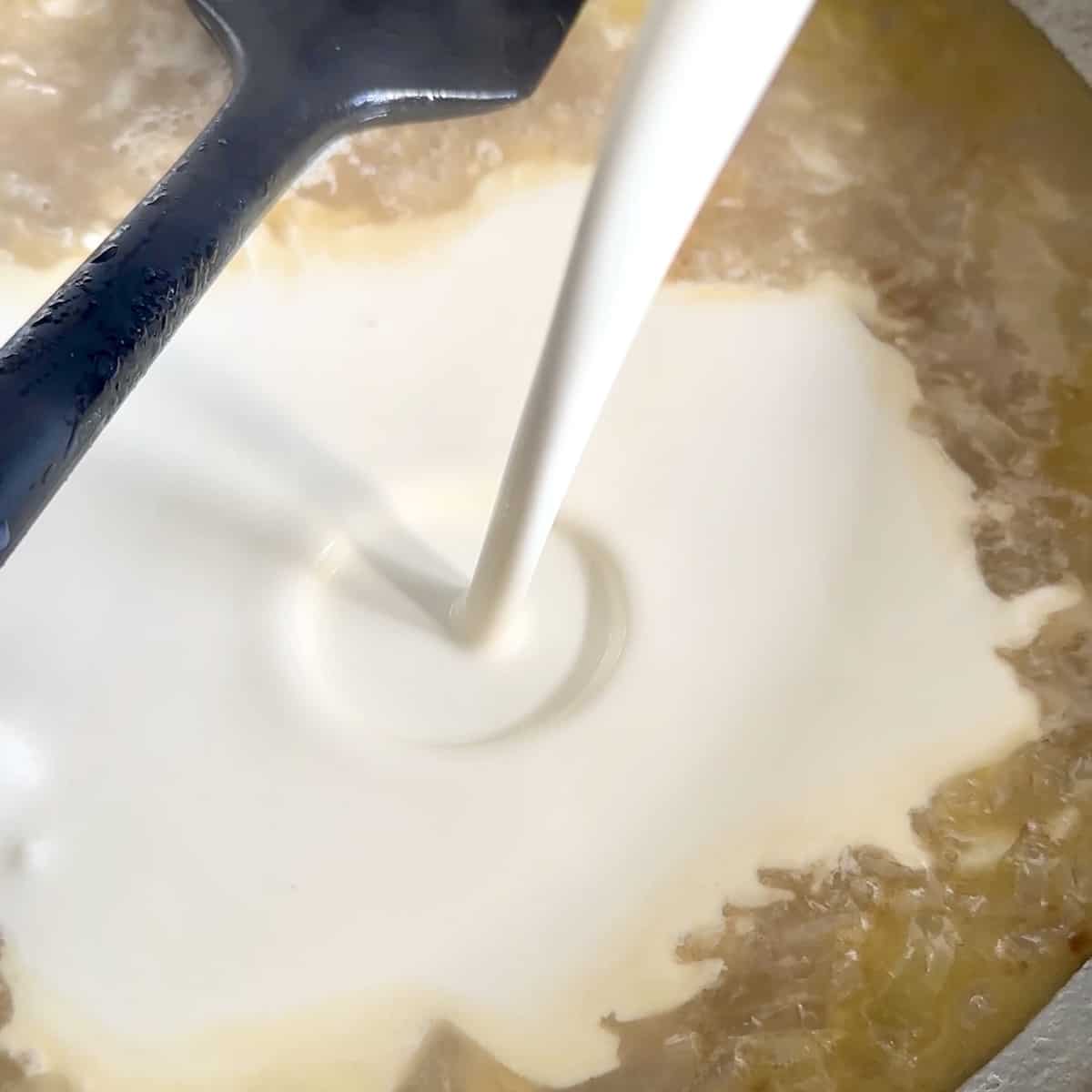 Cream being poured into mussels soup in a saucepan. 