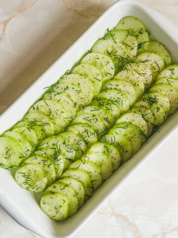 Sliced cucumber salad in a serving dish garnished with dill and black pepper.