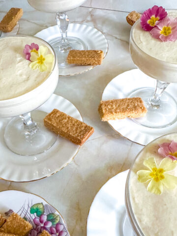 Coupe glasses with gooseberry fool in, decorated with edible flowers and with shortbread on the side.
