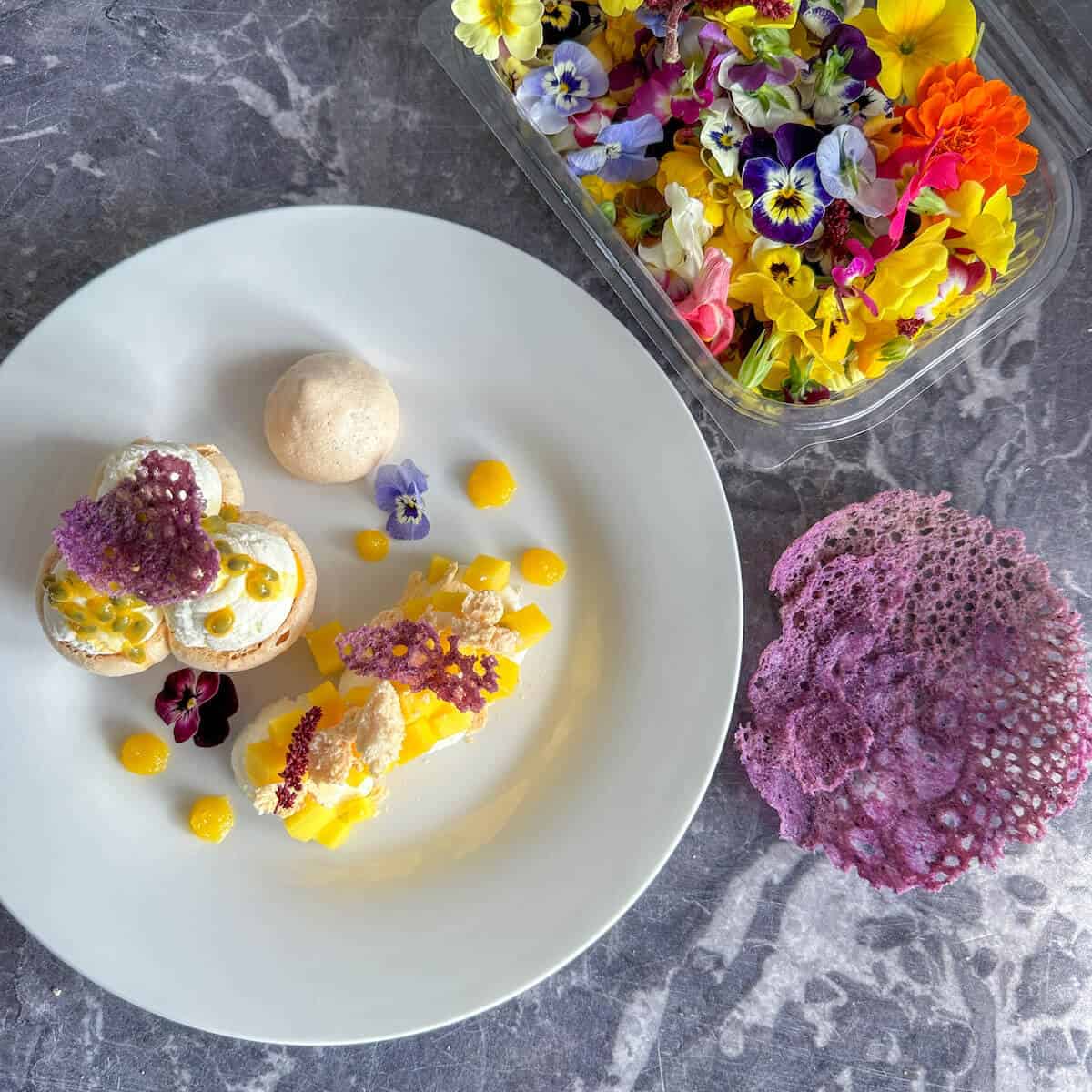 A box of edible flowers next to a plate of dessert.