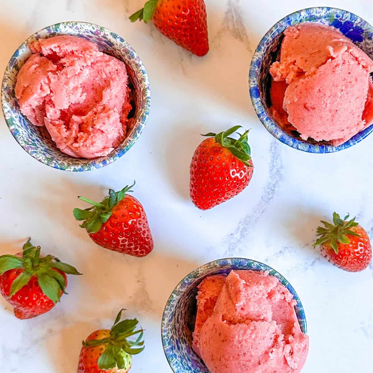Bowls of strawberry frozen yogurt surrounded by fresh strawberries. 