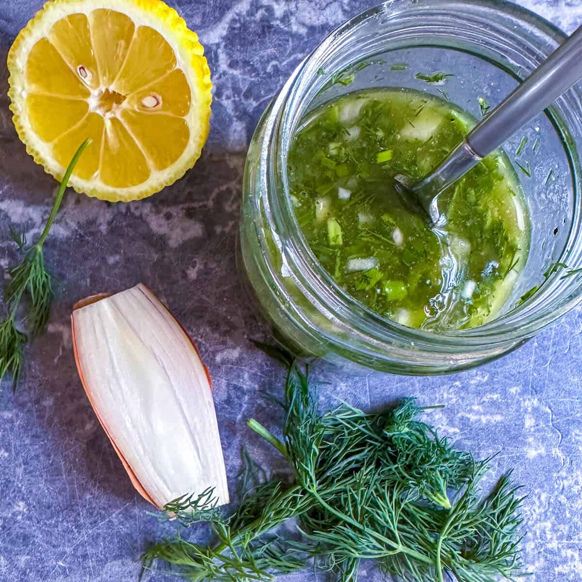 Lemon Herb Vinaigrette Dressing in a jar next to a lemon, shallot and some fresh herbs.