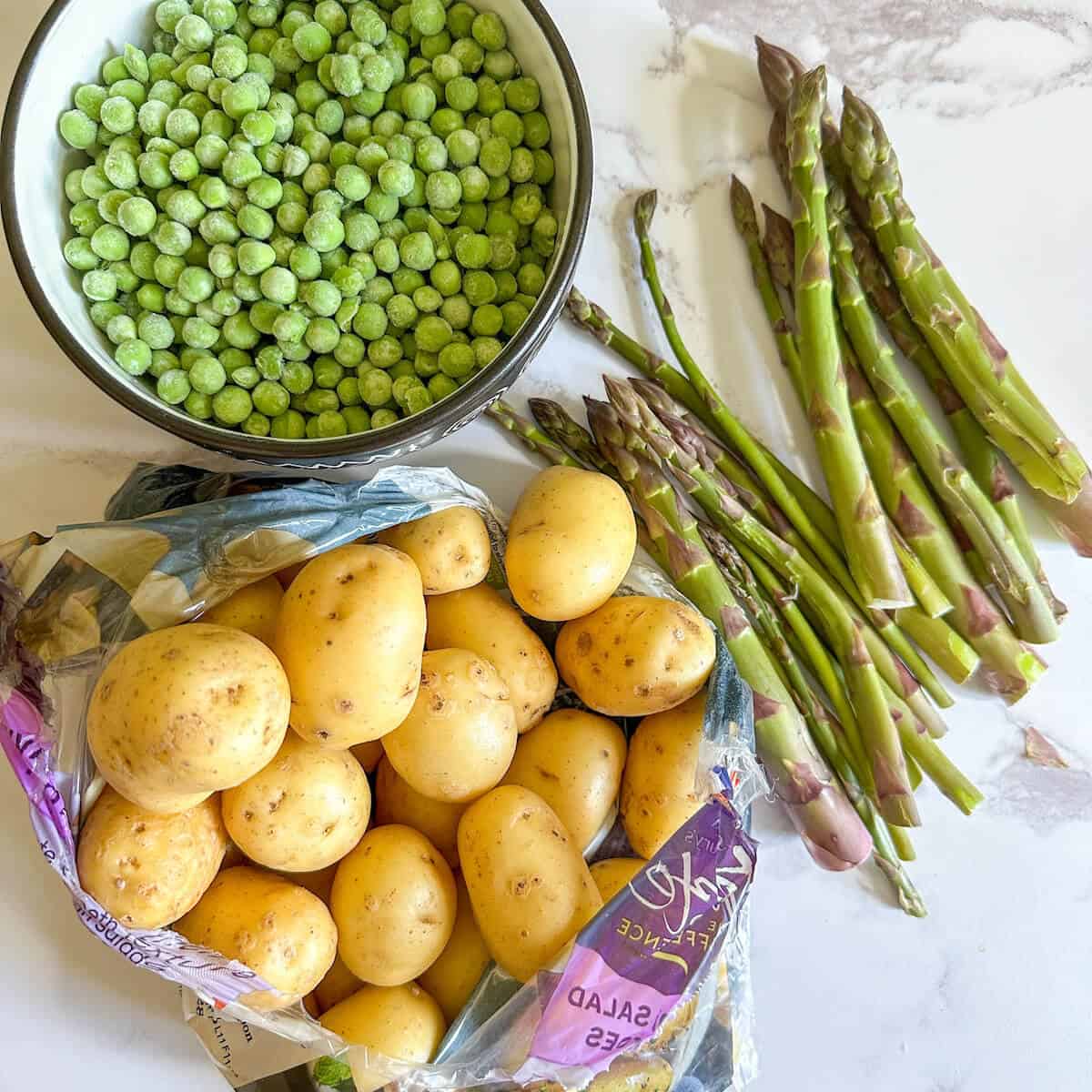 Potatoes, peas and asparagus on a work surface. 