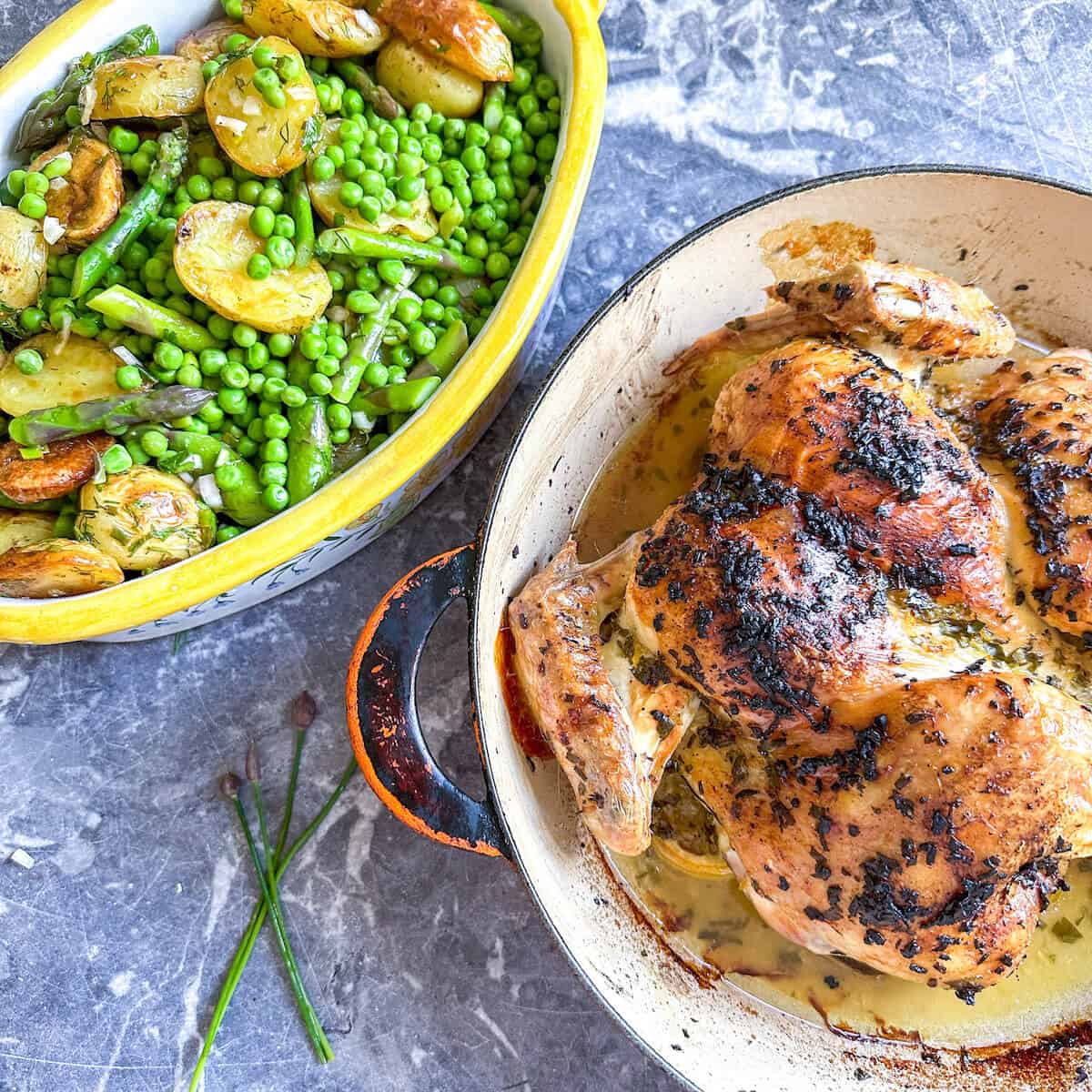 A serving dish of asparagus and potato salad next to a roasted chicken.
