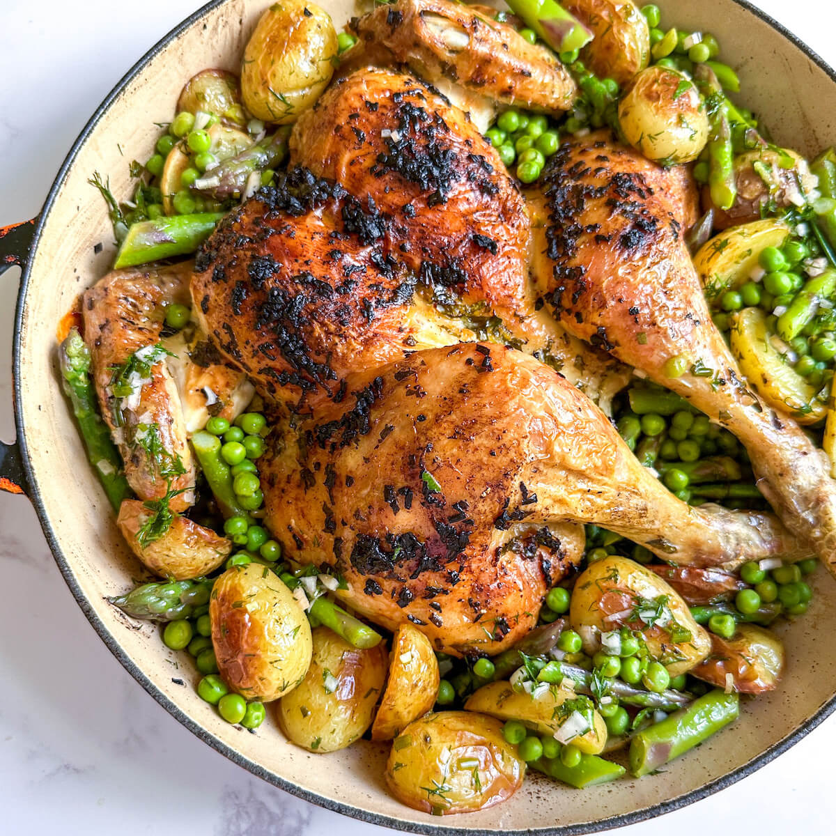 Roasted citrus and herb spatchcock chicken in a shallow dish surrounded by spring vegetables. 