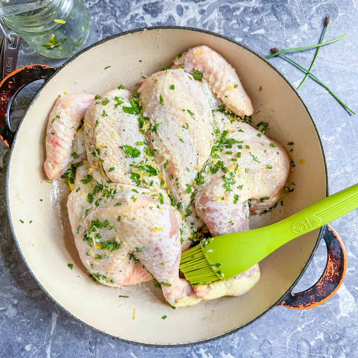 A spatchcock chicken being brushed with citrus herb marinade before roasting.