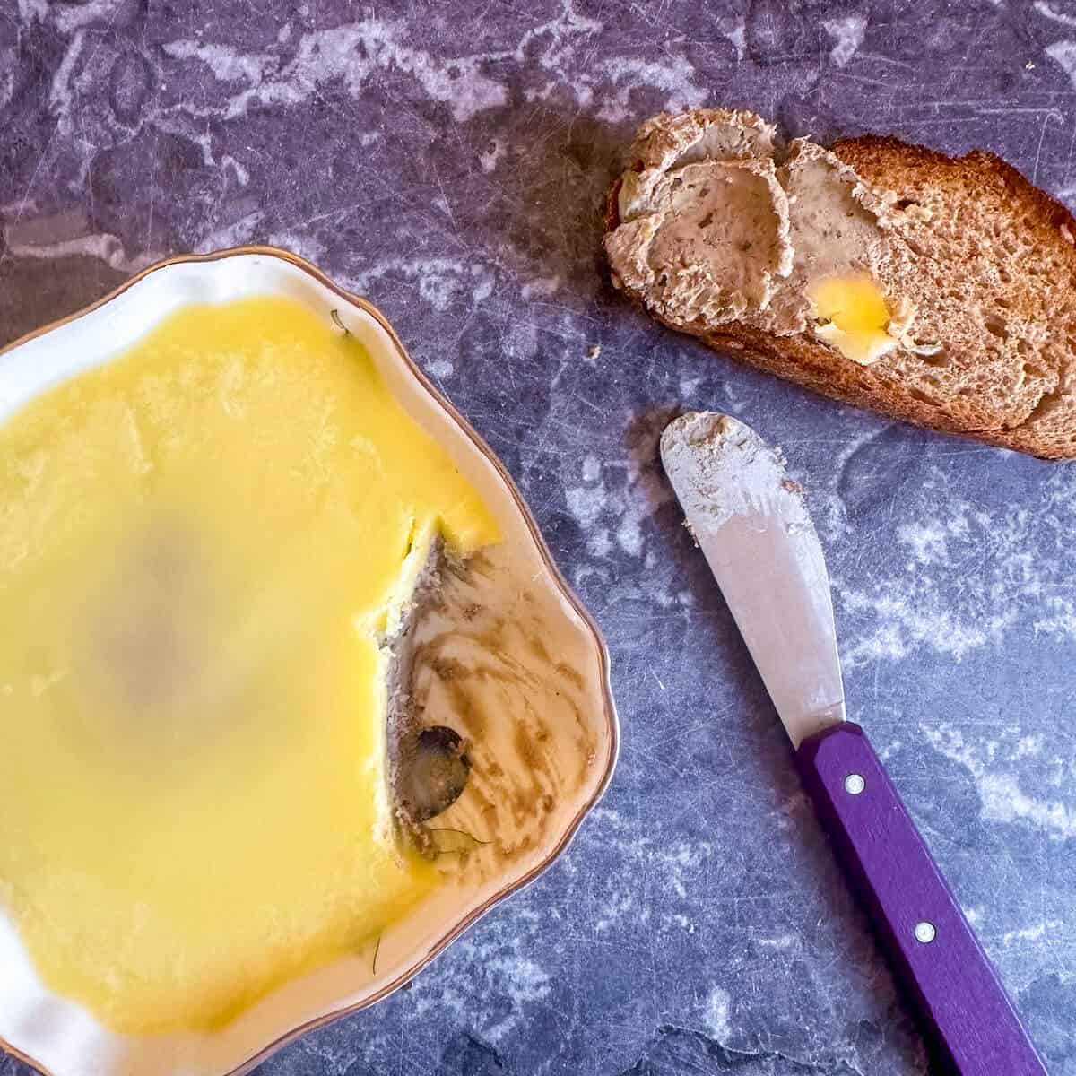 Duck liver pate in a dish next to a butter knife and a piece of toast.