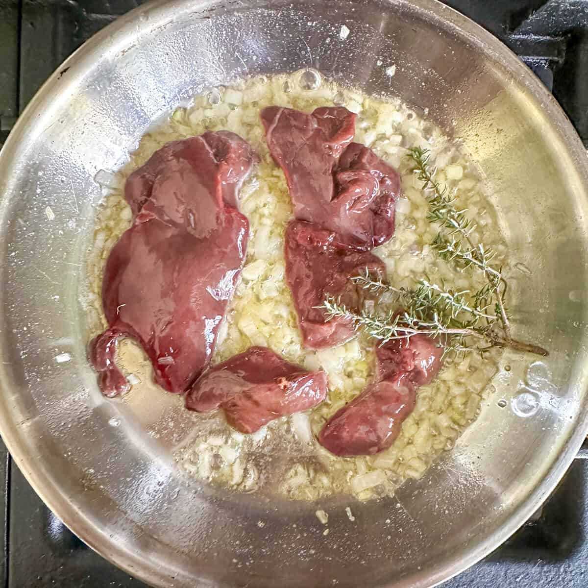 a shallow frying pan with duck liver and shallots being fried in butter, with garlic and thyme. 
