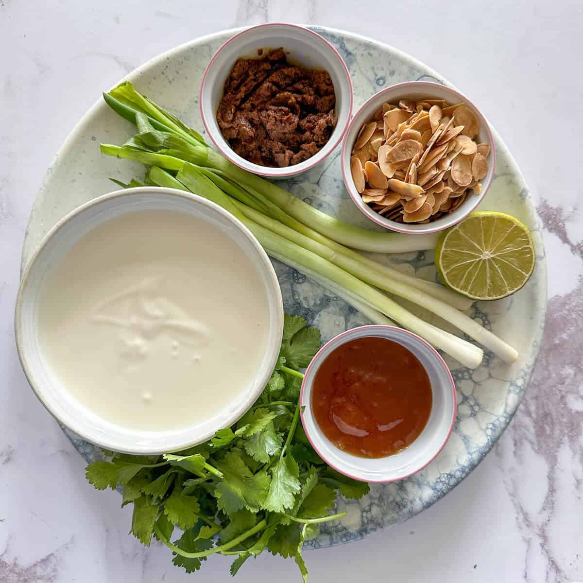 The chicken coronation sauce ingredients on a tray. Yogurt, mayo, curry paste, lime, spring onion, flaked almonds, coriander and mango chutney. 