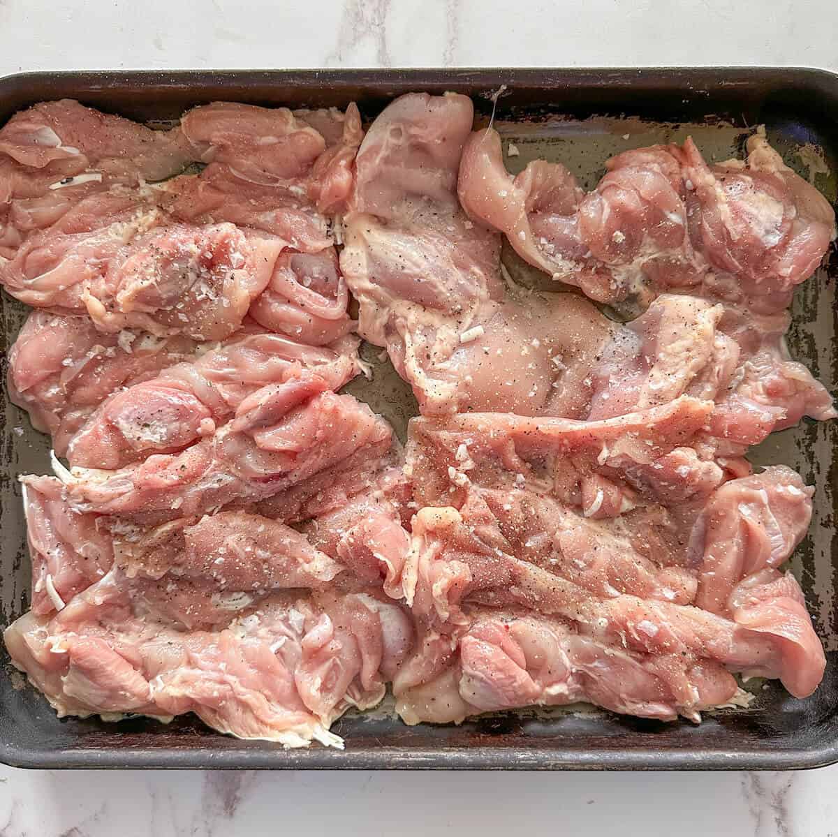 Raw boneless chicken thighs on an oven tray. 