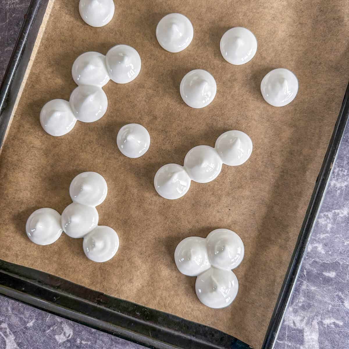 A baking tray with several piped mounds of raw meringue on it. 