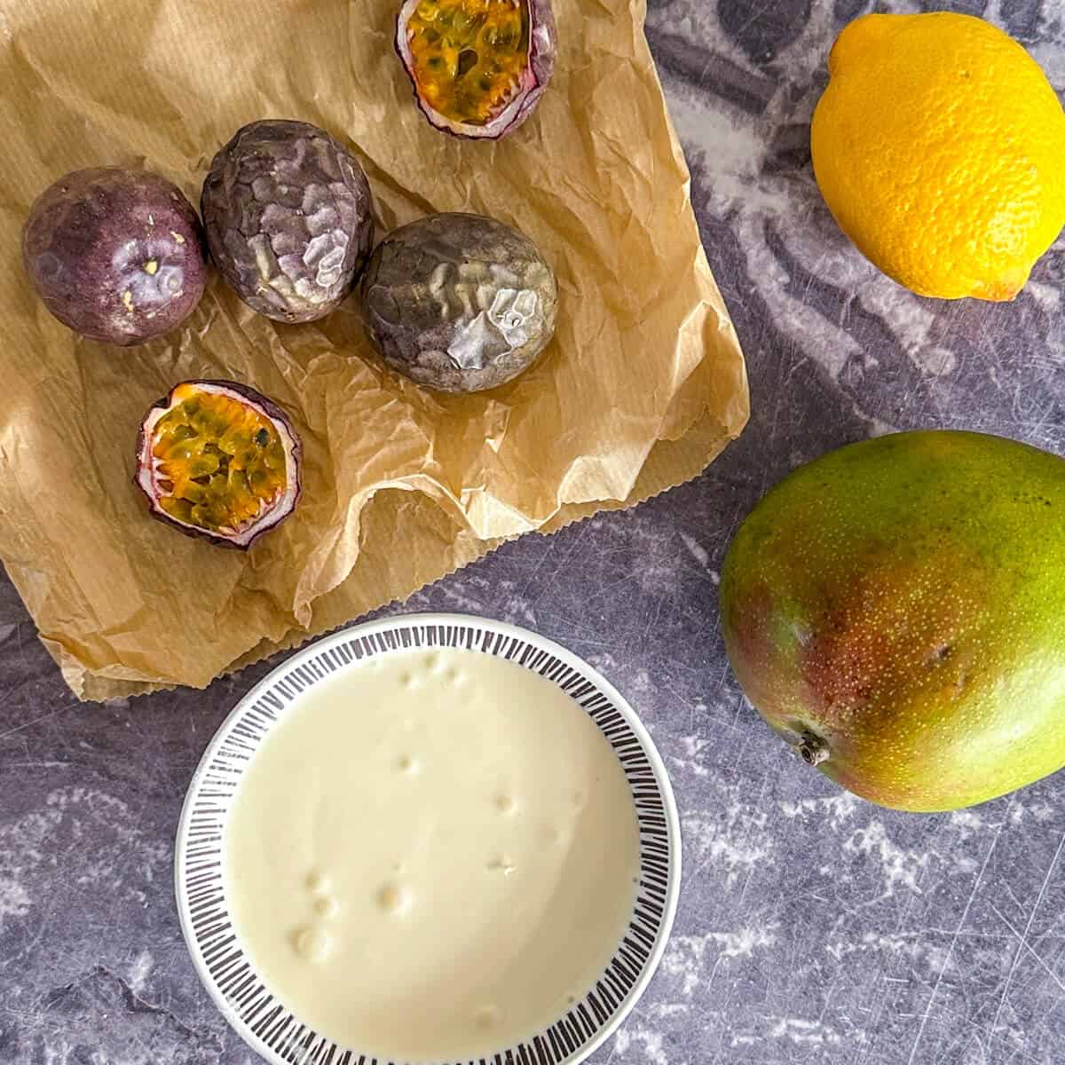 A bowl of cream, next to a mango, a lemon and several passion fruit. 