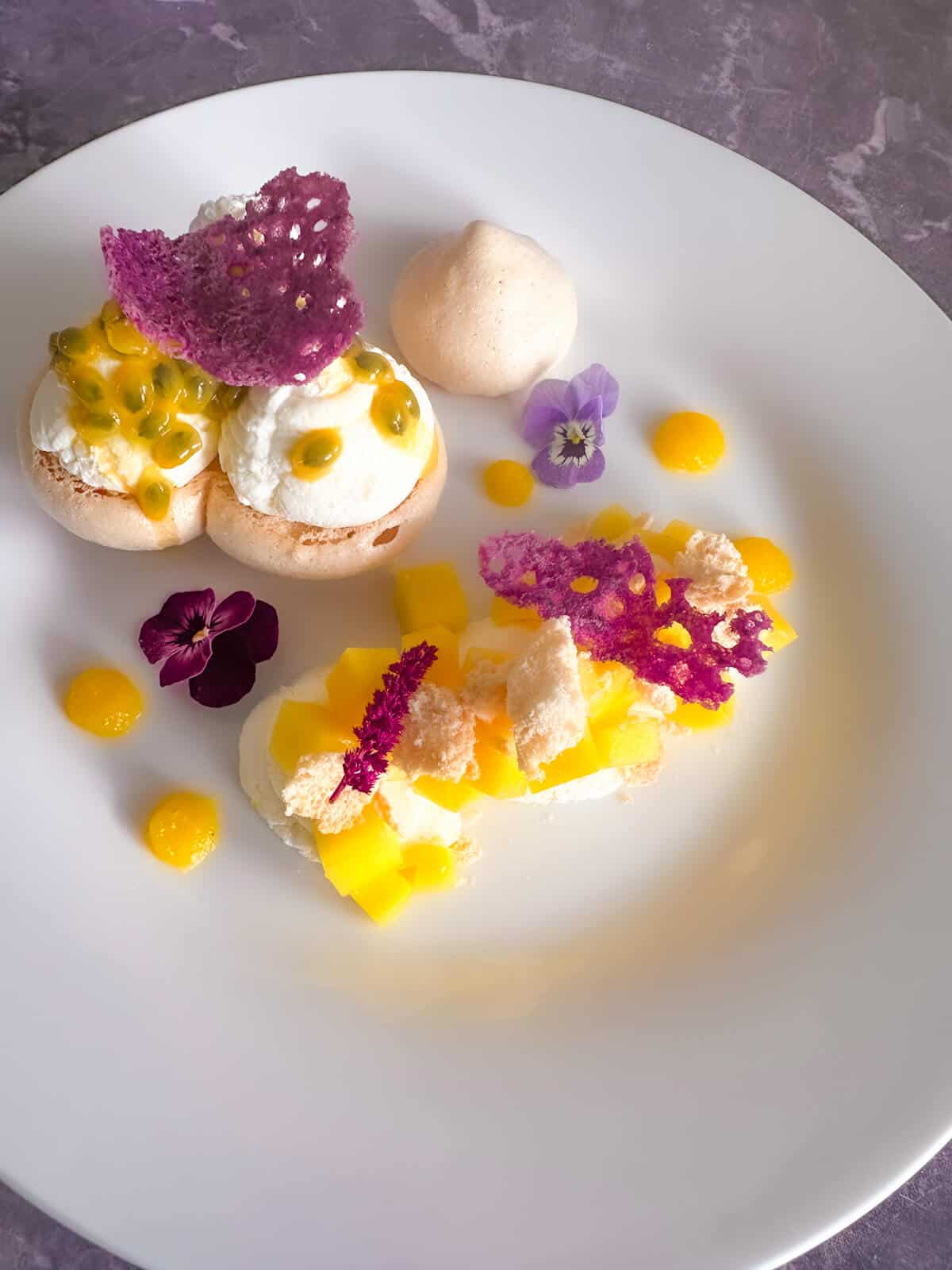 Mango Passion Fruit Eton Mess on a plate garnished with crumbled meringue and edible flowers. 