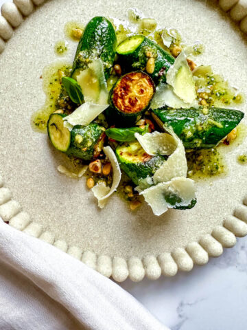Sautéed Italian Zucchini on a plate topped with shaved parmesan and and Hazelnut Pesto.