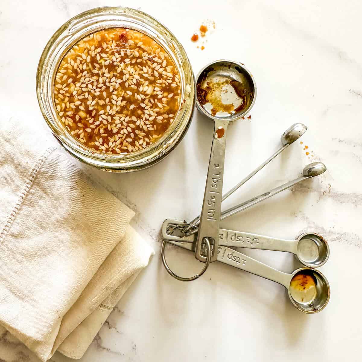 A jar of sesame miso dressing next to a set of measuring spoons and a napkin. 