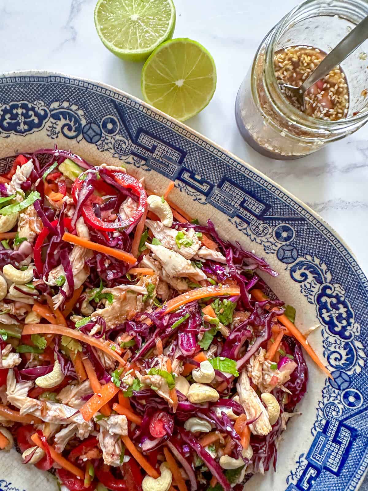 A serving dish of colorful shredded vegetable salad next to a jar of sesame miso dressing. 