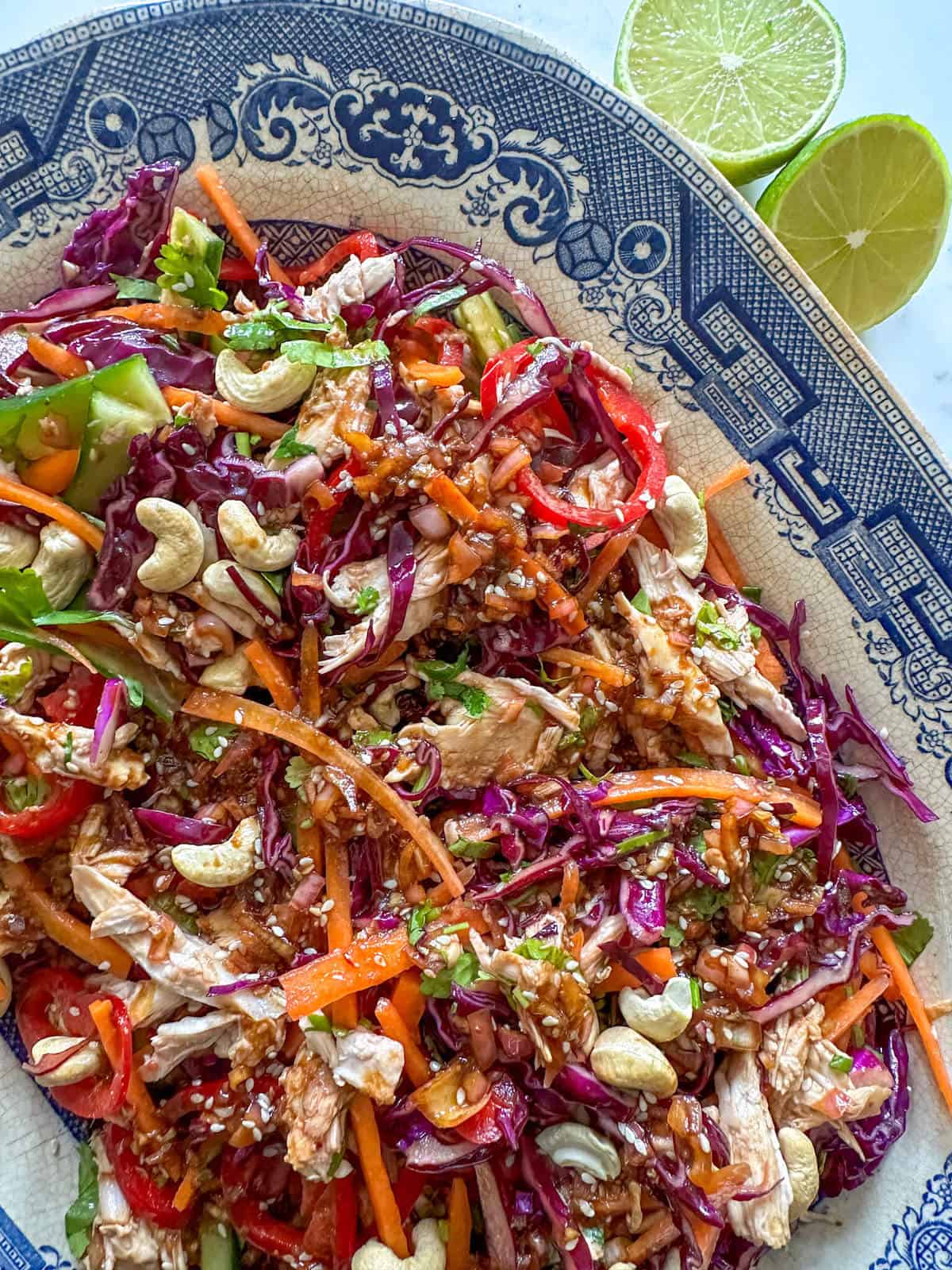 A large platter of chicken salad with chopped raw vegetables and fresh limes. 