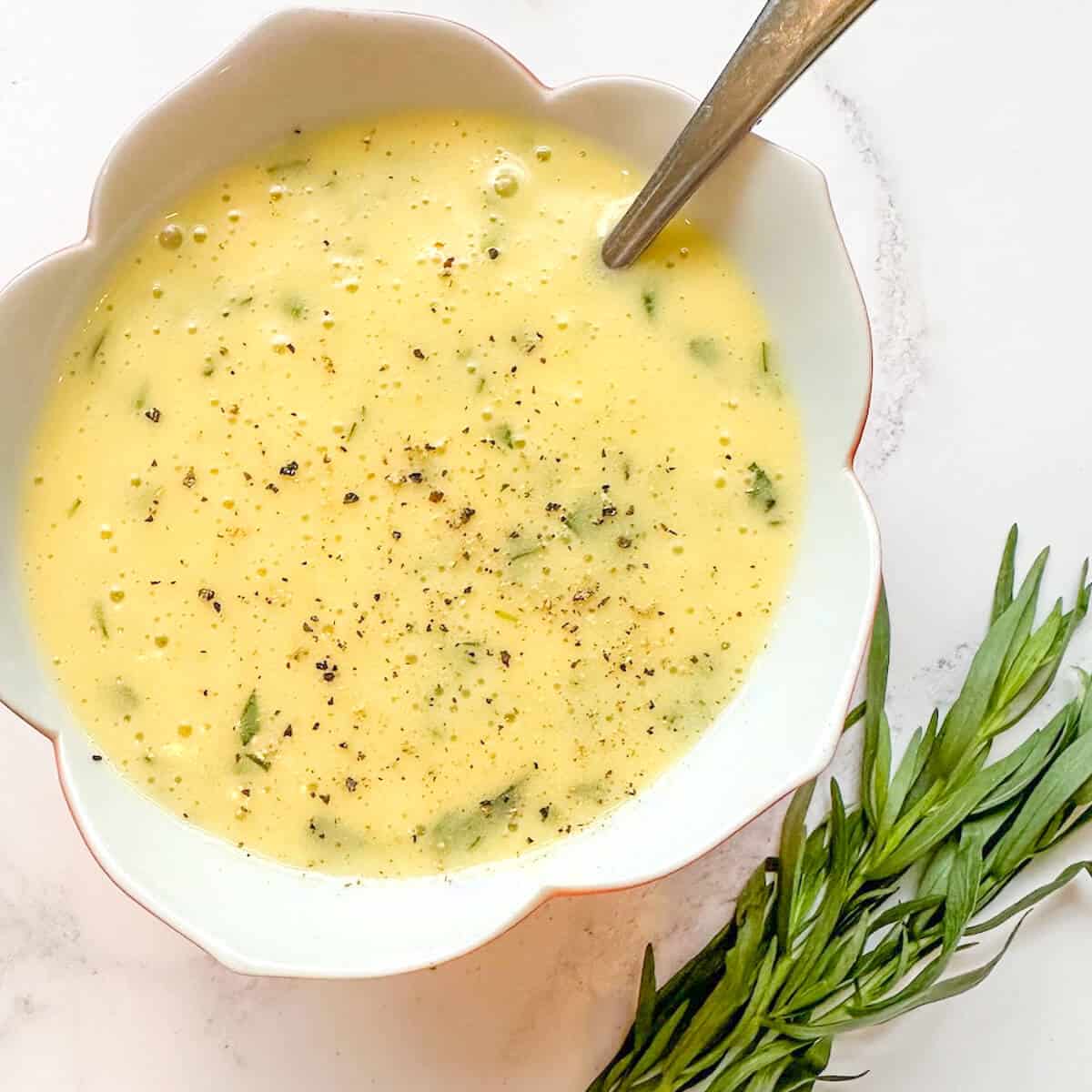 A serving dish of bearnaise sauce with a spoon. 