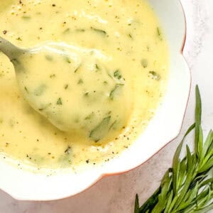 Bearnaise sauce in a dish next to a small bunch of fresh tarragon.