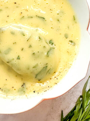 Bearnaise sauce in a dish next to a small bunch of fresh tarragon.