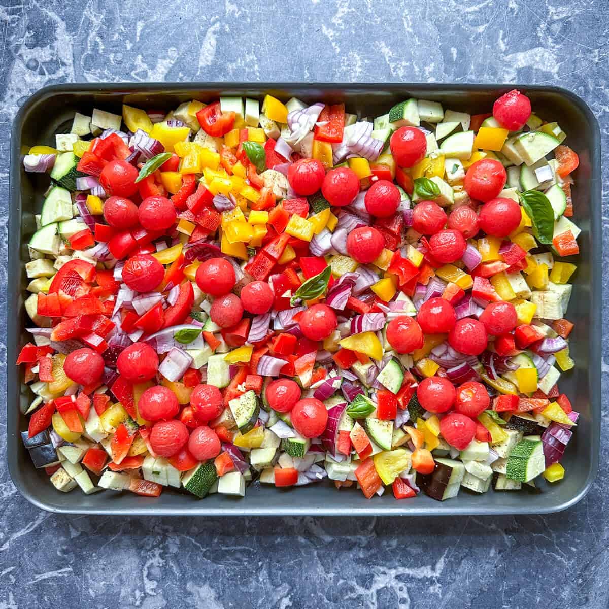 A deep oven tray with prepped ratatouille vegetables ready to roast. 