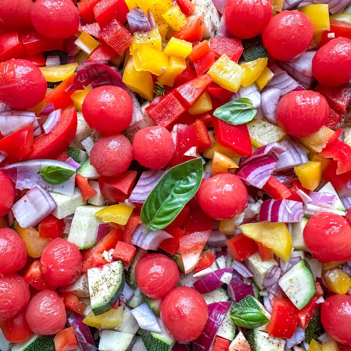 A close up image of chopped vegetables and fresh basil, prepped for ratatouille. 