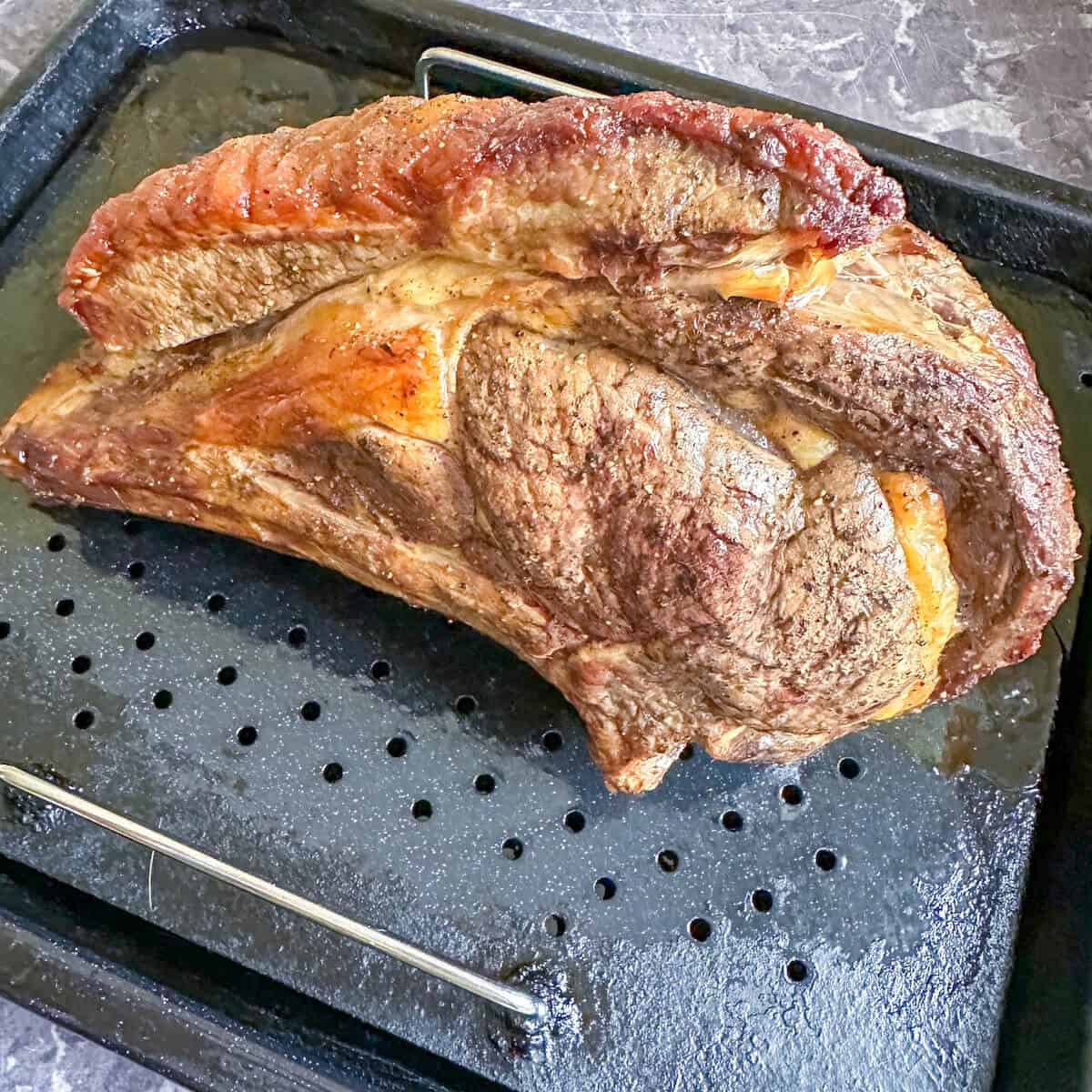A cooked standing rib roast on a roasting tray. 