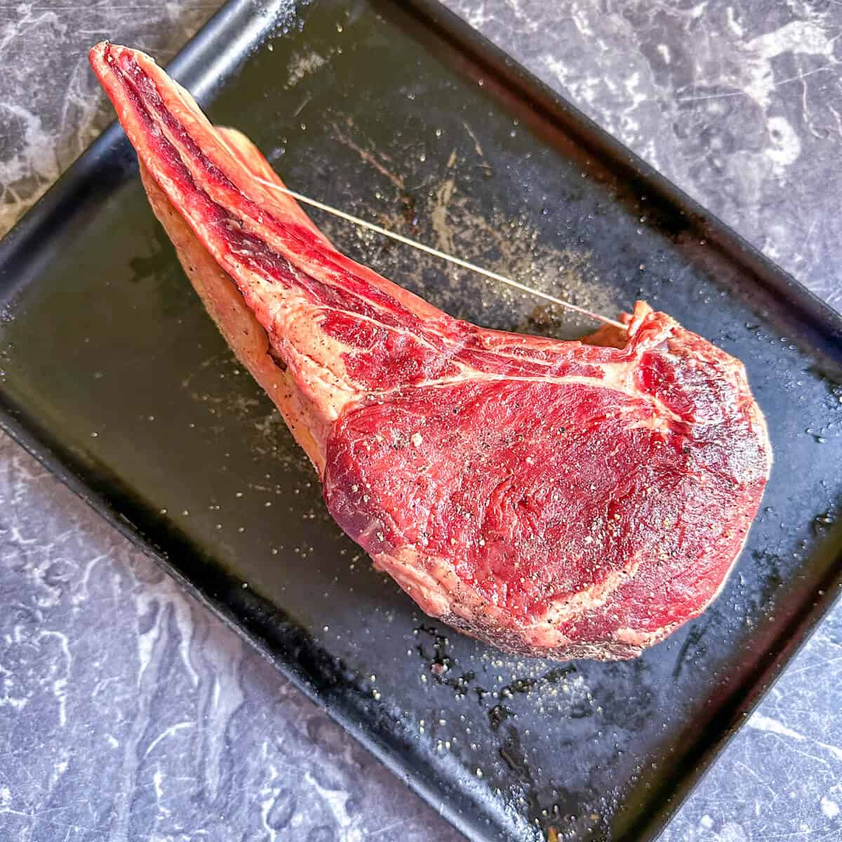 A piece of raw prime rib on the bone on an oven tray. 