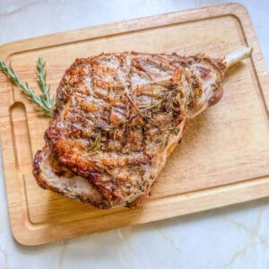 Crispy roast lamb leg on a wooden chopping board.