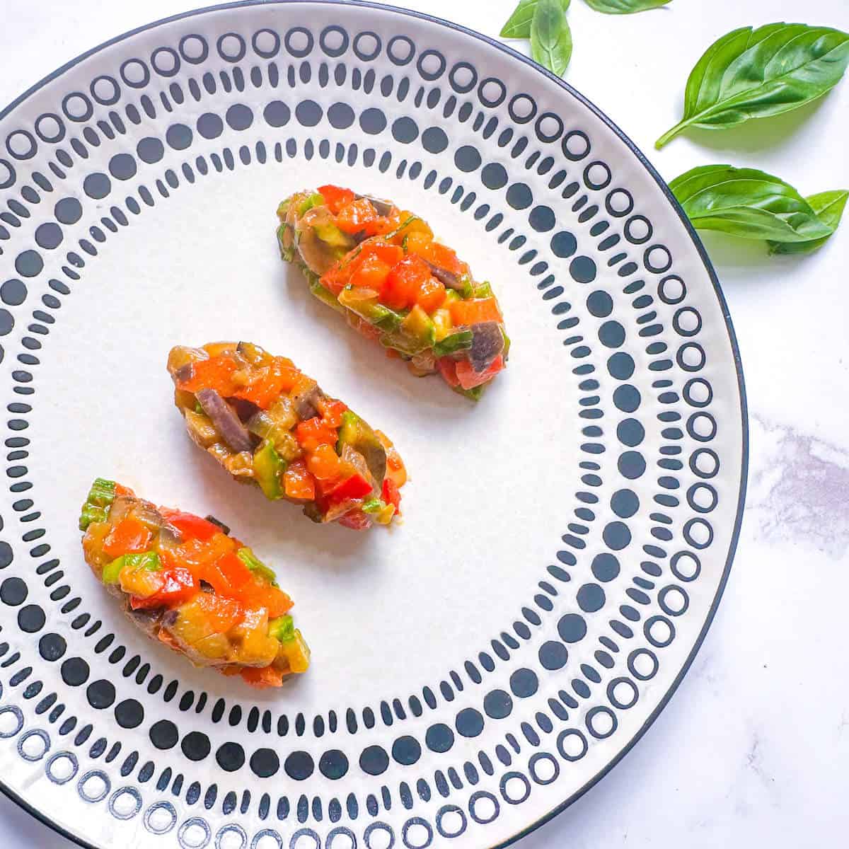 Gourmet ratatouille quenelles on a plate next to some fresh basil. 