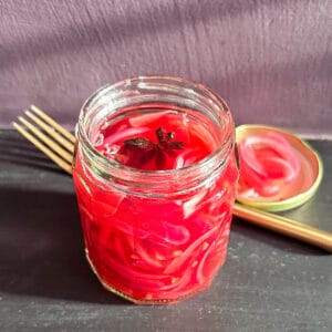 Pickled red onions in a jar on a worktop.