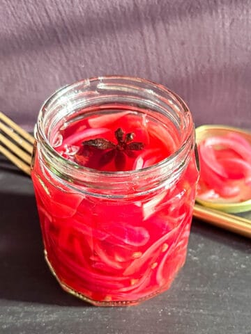 Pickled red onions in a jar on a worktop.