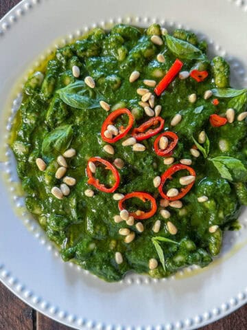 White beans with cavolo nero pesto on a white plate topped with chili peppers and pine nuts.