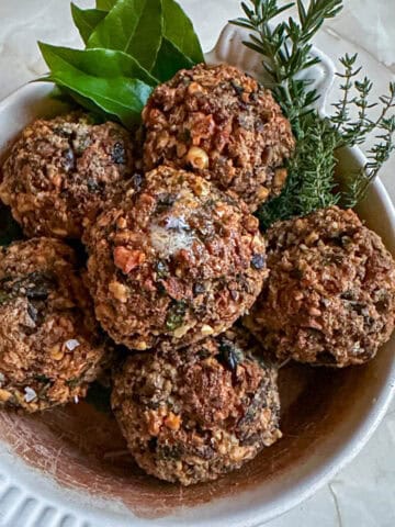 Walnut and portobello mushroom stuffing balls in a serving dish with fresh herbs.