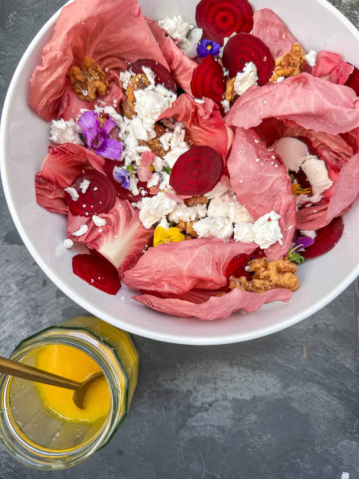 A bowl of beetroot carpaccio salad next to a jar of orange vinaigrette. 