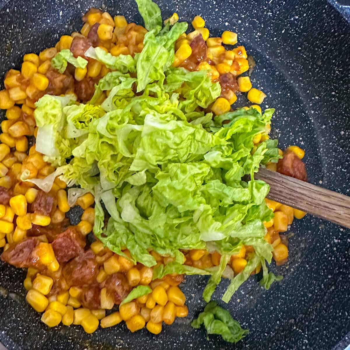 Corn fricassee in a frying pan with little gem lettuce. 