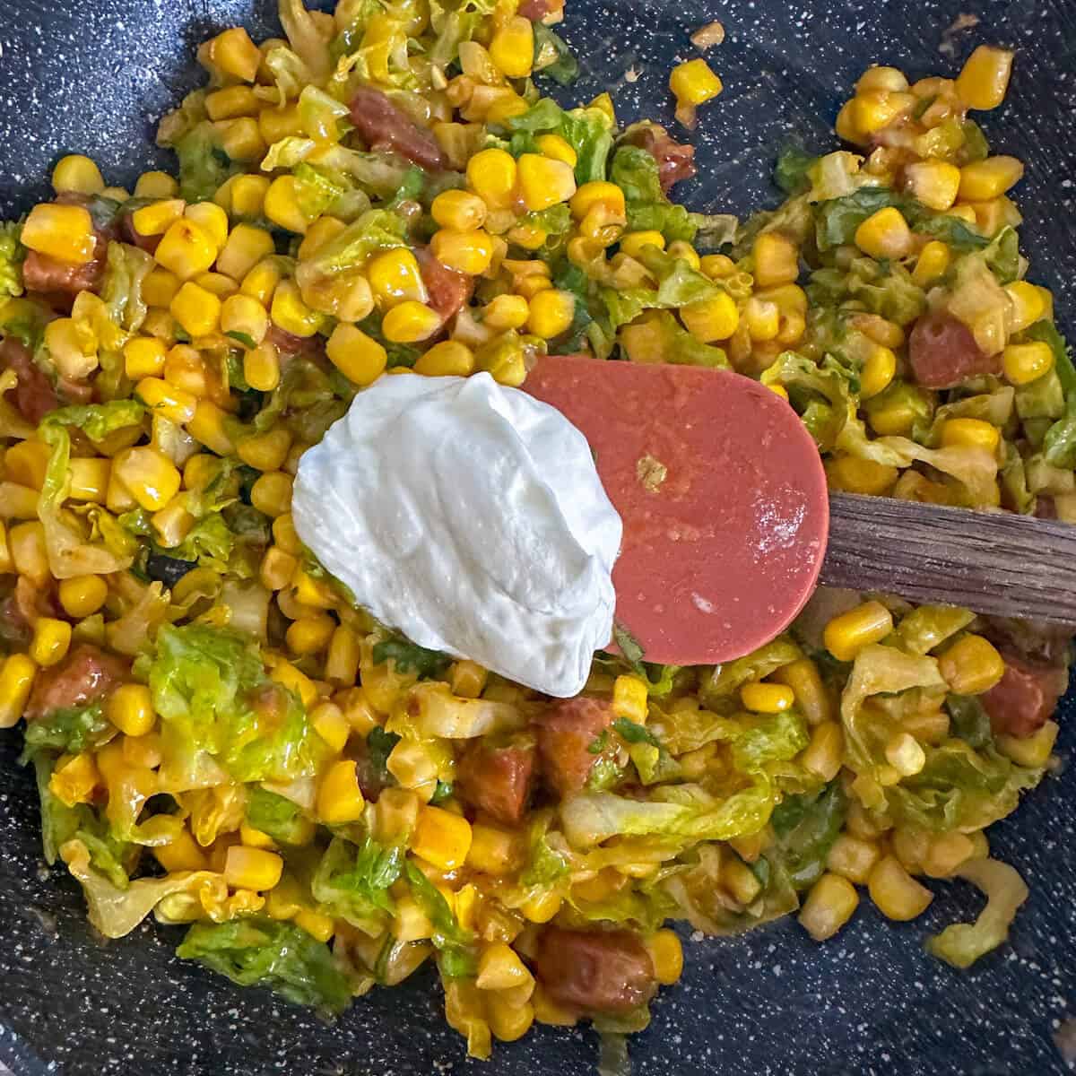 A corn fricassee cooking in a pan with a spoonful of creme fraiche. 