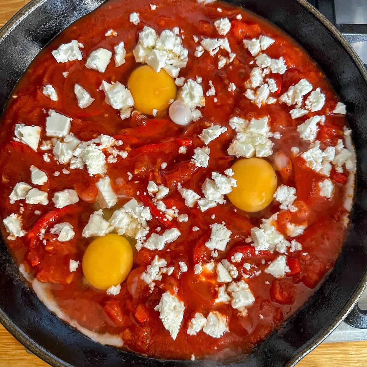 Huevos Rancheros about to go in the oven with raw eggs in a tomato based sauce in a skillet. 