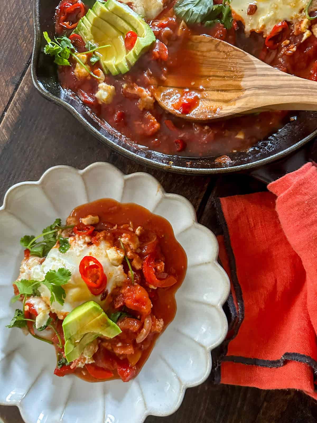A serving of huevos rancheros on a plate next to a skillet. 