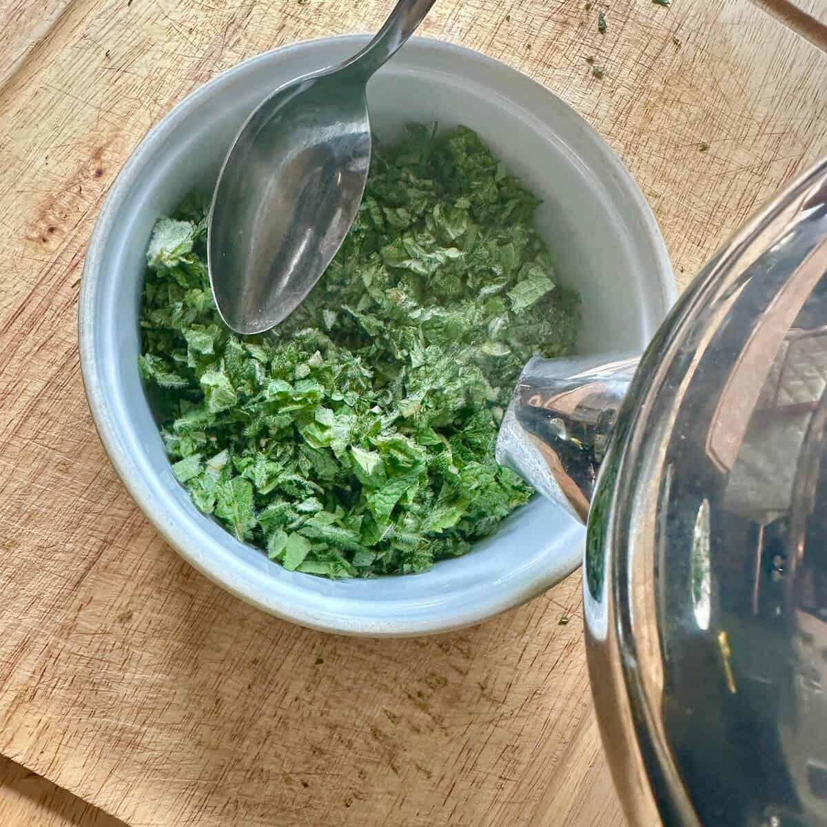 Boiled water being poured over fresh mint in a bowl to make mint sauce. 