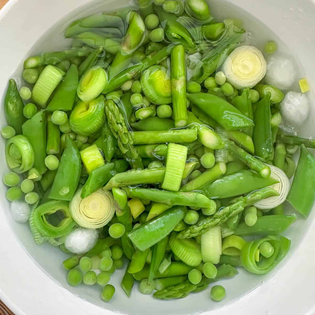 A bowl of ice water containing blanched spring vegetables. 